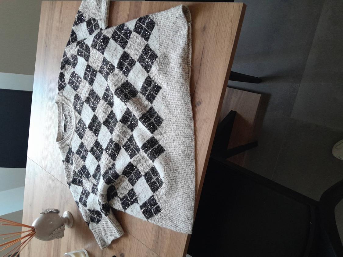 Black and white argyle knit jumper on a wooden table, next to a decorative vase.
