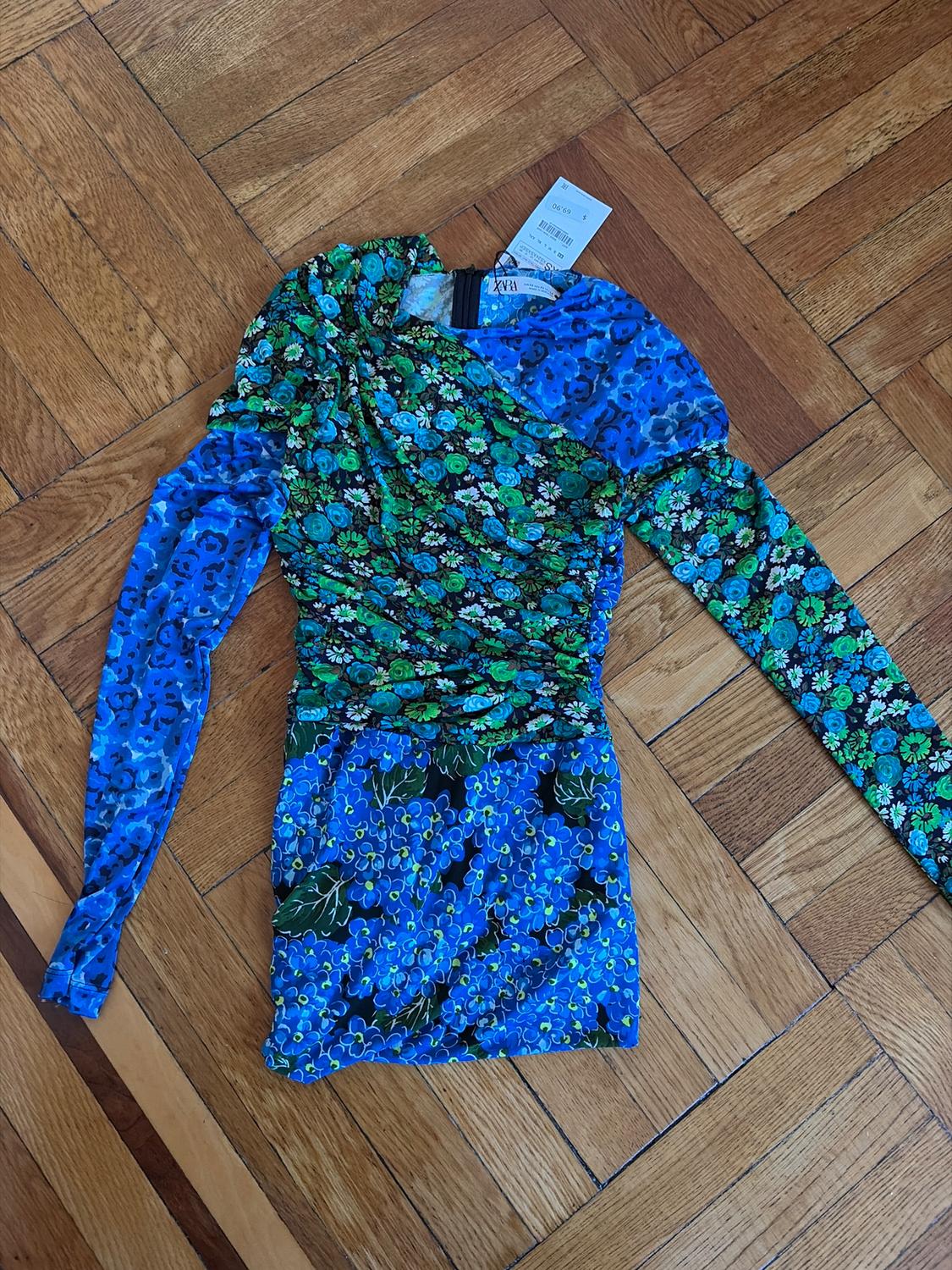 Short-sleeved dress with blue and green floral print on a wooden floor. Visible label on the collar.