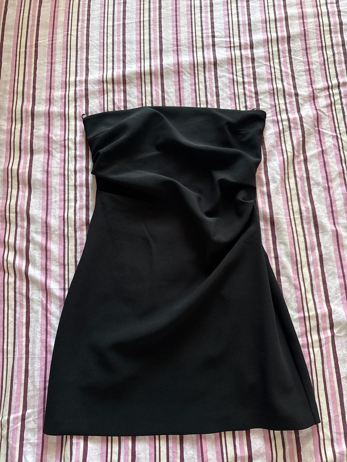 Black strapless mini dress with ruching, against a fabric background with pink, purple, and white vertical stripes.