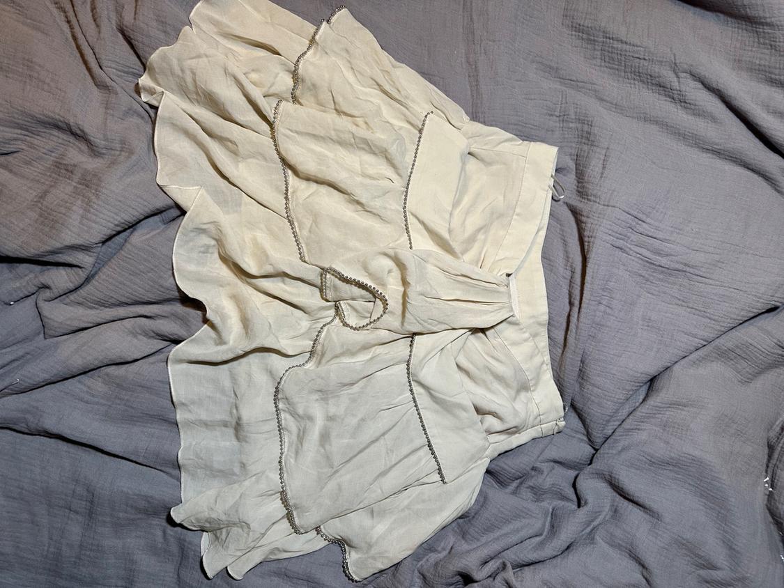 White skirt with ruffles and dark trim over wrinkled grey fabric. The texture and design create a relaxed and casual style.