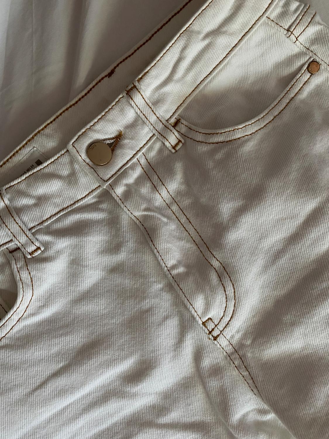 Detail of white denim with brown contrast stitching and a gold button, on a white sheet. Casual and relaxed style.