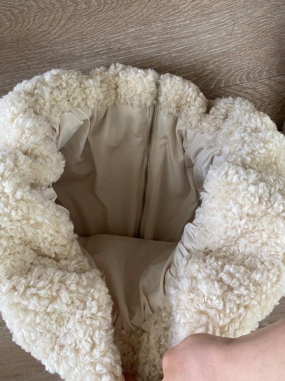 Soft and fluffy cream fabric bag, open and viewed from above, with a visible zipper closure inside.