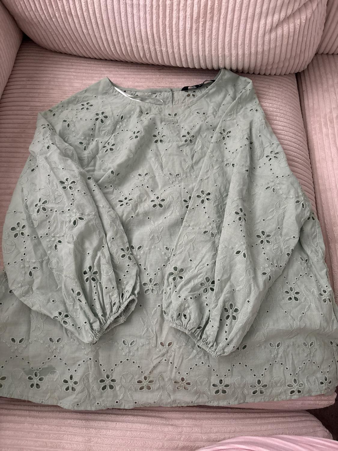 Light green blouse with openwork floral embroidery and long puff sleeves, on a pink corduroy sofa.