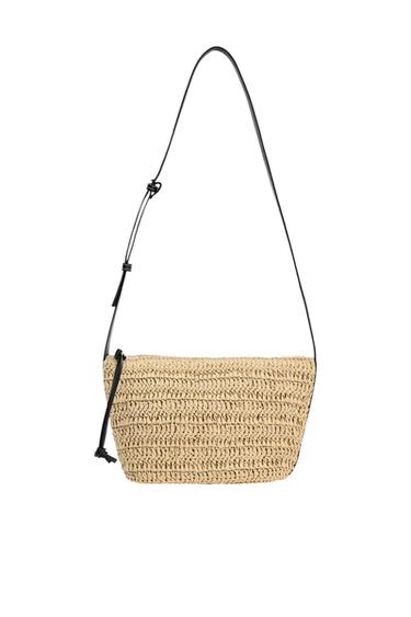 Natural-colored woven raffia shoulder bag with a thin black strap and side knot detail, on a white background.