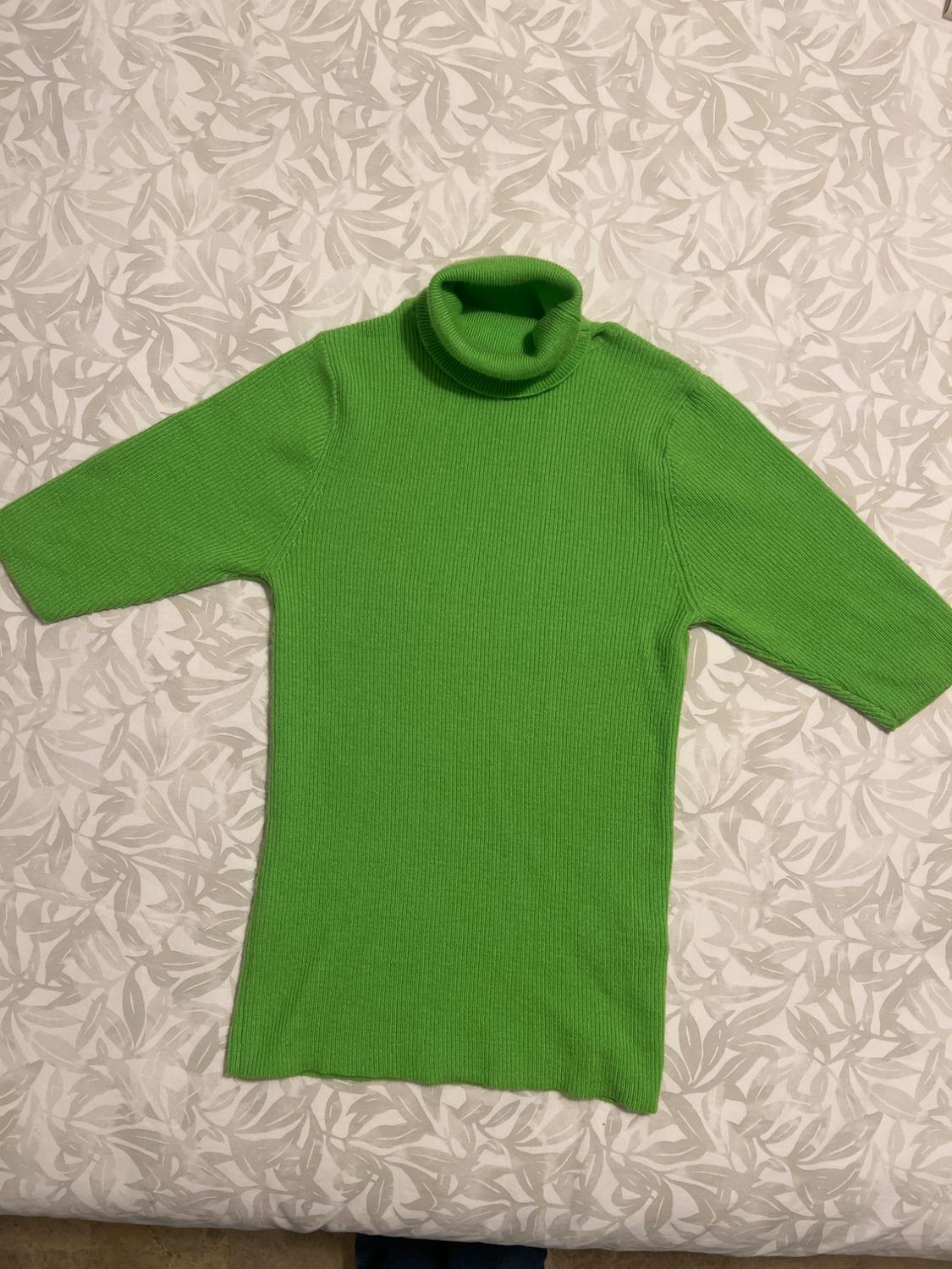 Green polo neck, three-quarter sleeve jumper over a light-toned, leaf-patterned fabric.