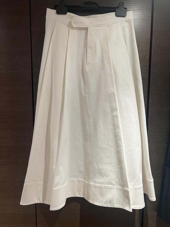 White pleated skirt hanging on a black hanger, against a dark wooden background.