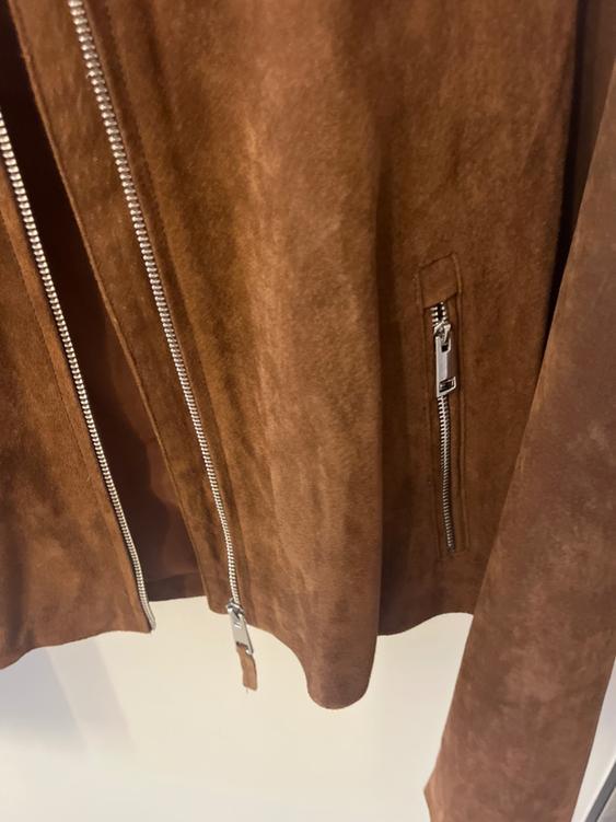 Brown suede jacket with visible silver zippers on a white background. Closure detail and soft texture.