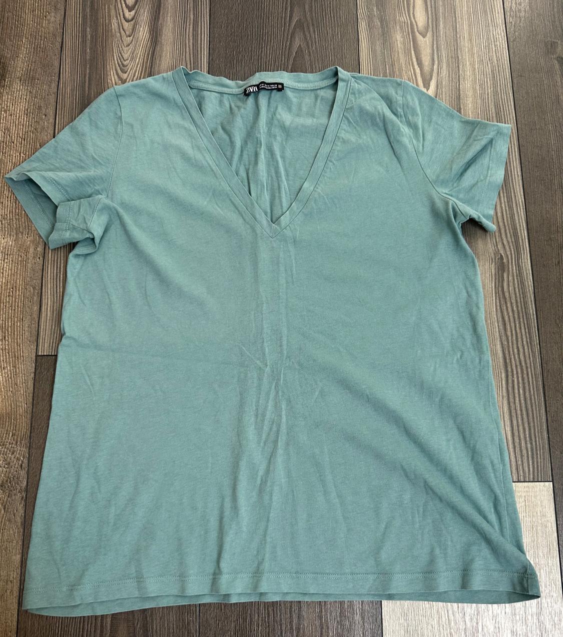 Light green short-sleeved V-neck t-shirt, laid out on a wooden floor. Text visible on the label: ZARA.