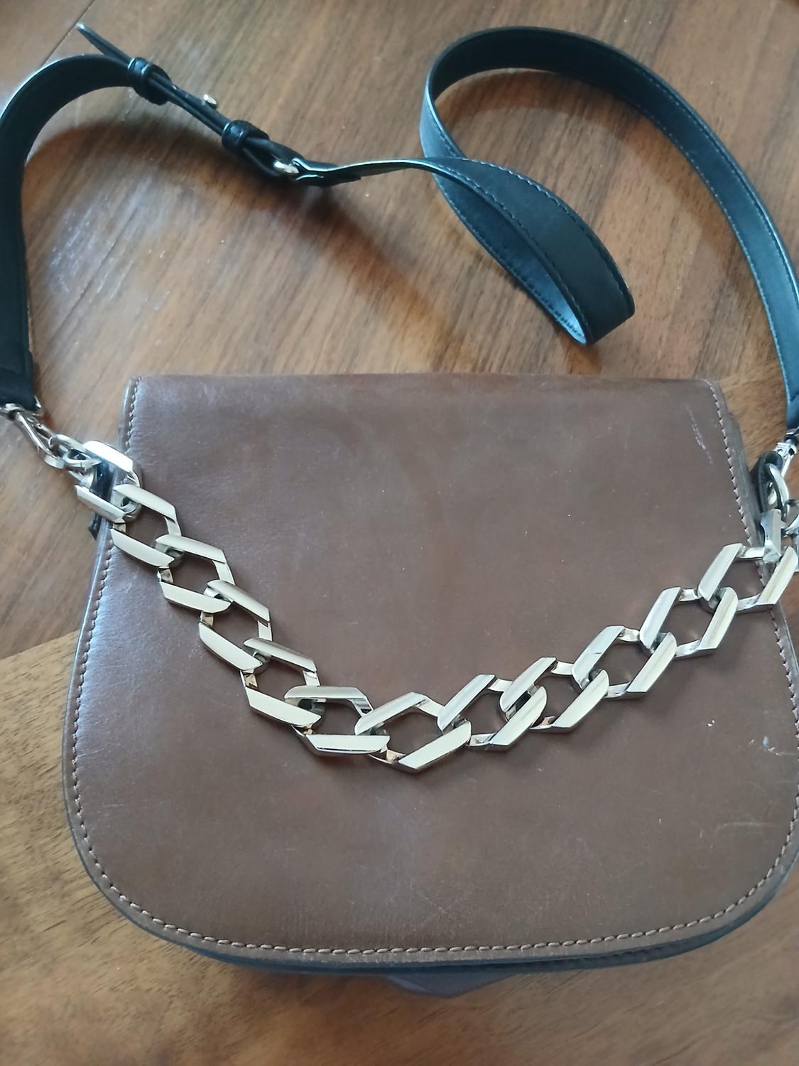 Close-up of a brown handbag with a decorative silver chain and a black strap.