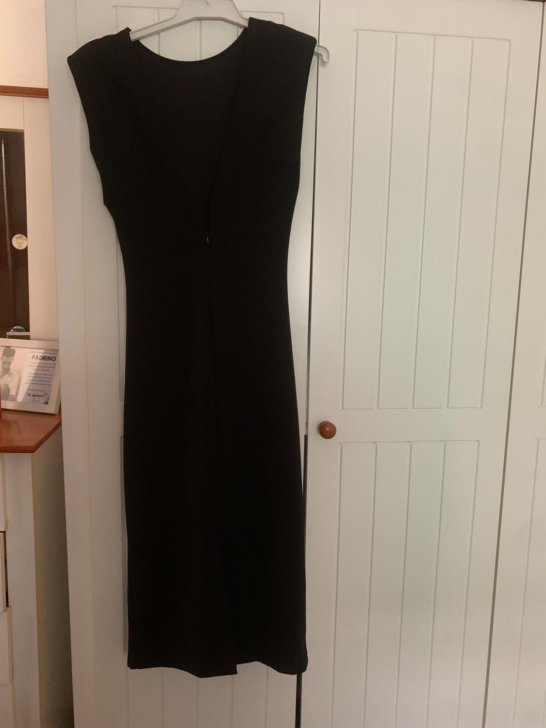 Sleeveless black dress hanging on a hanger in front of a white wardrobe. Background with wooden furniture details.