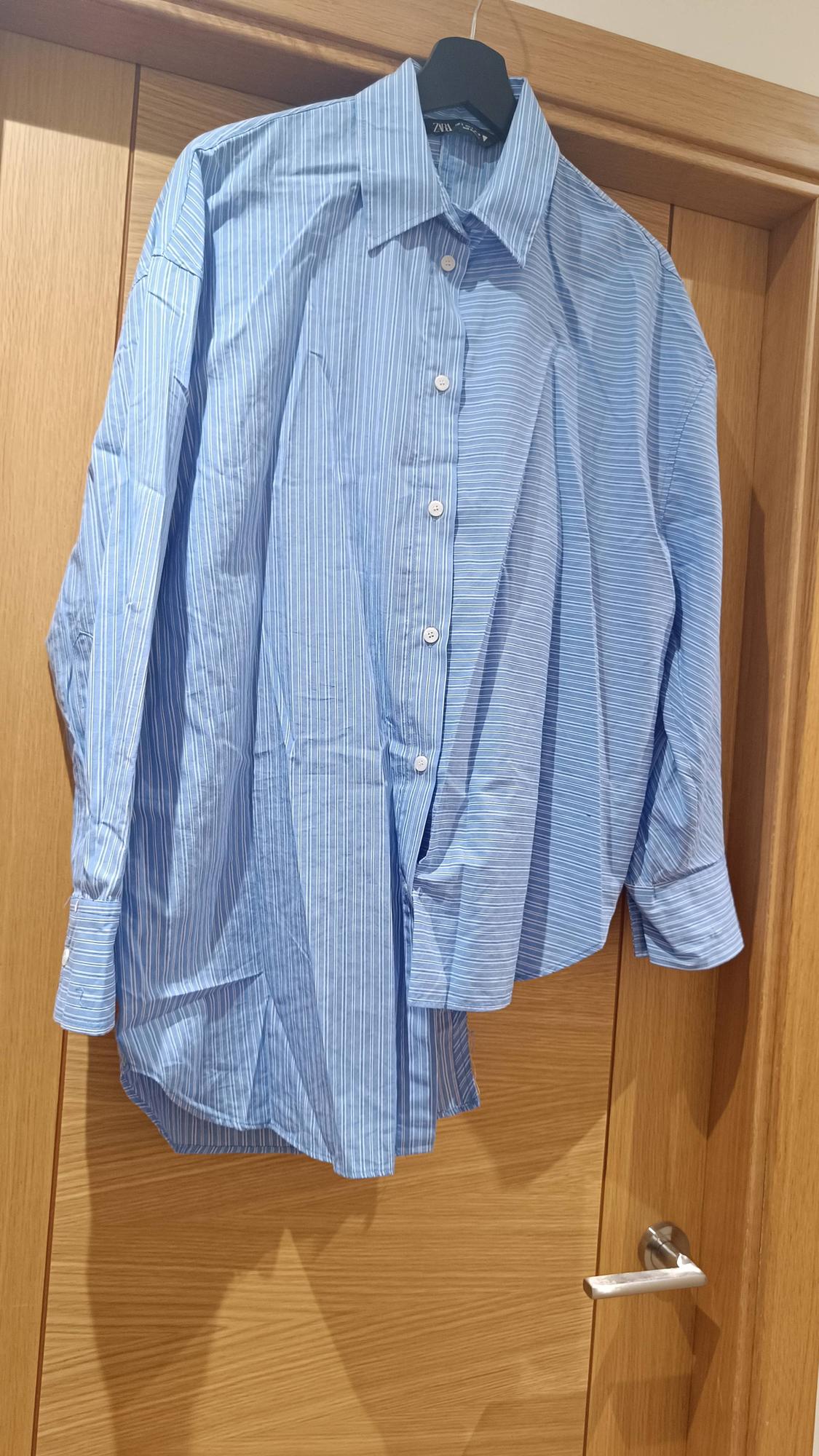 A blue shirt with white stripes hanging on a black hanger over a wooden door.