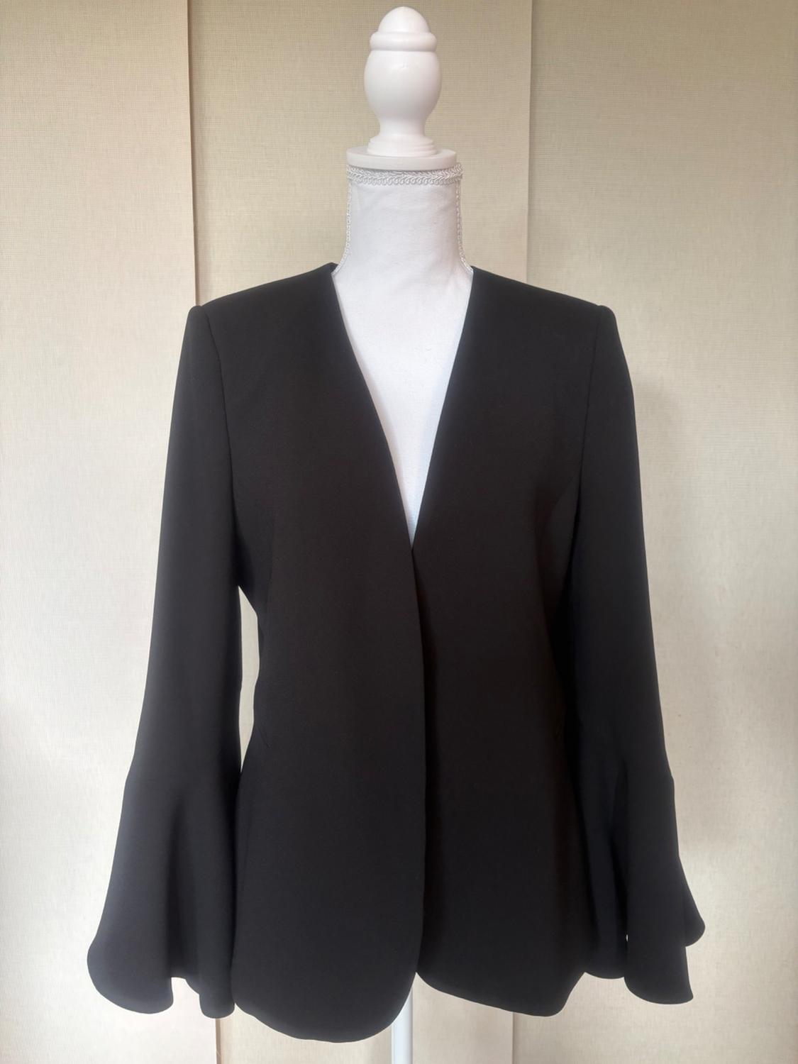 White mannequin wearing a black collarless jacket with a V-neck and flared cuff sleeves against a light background.