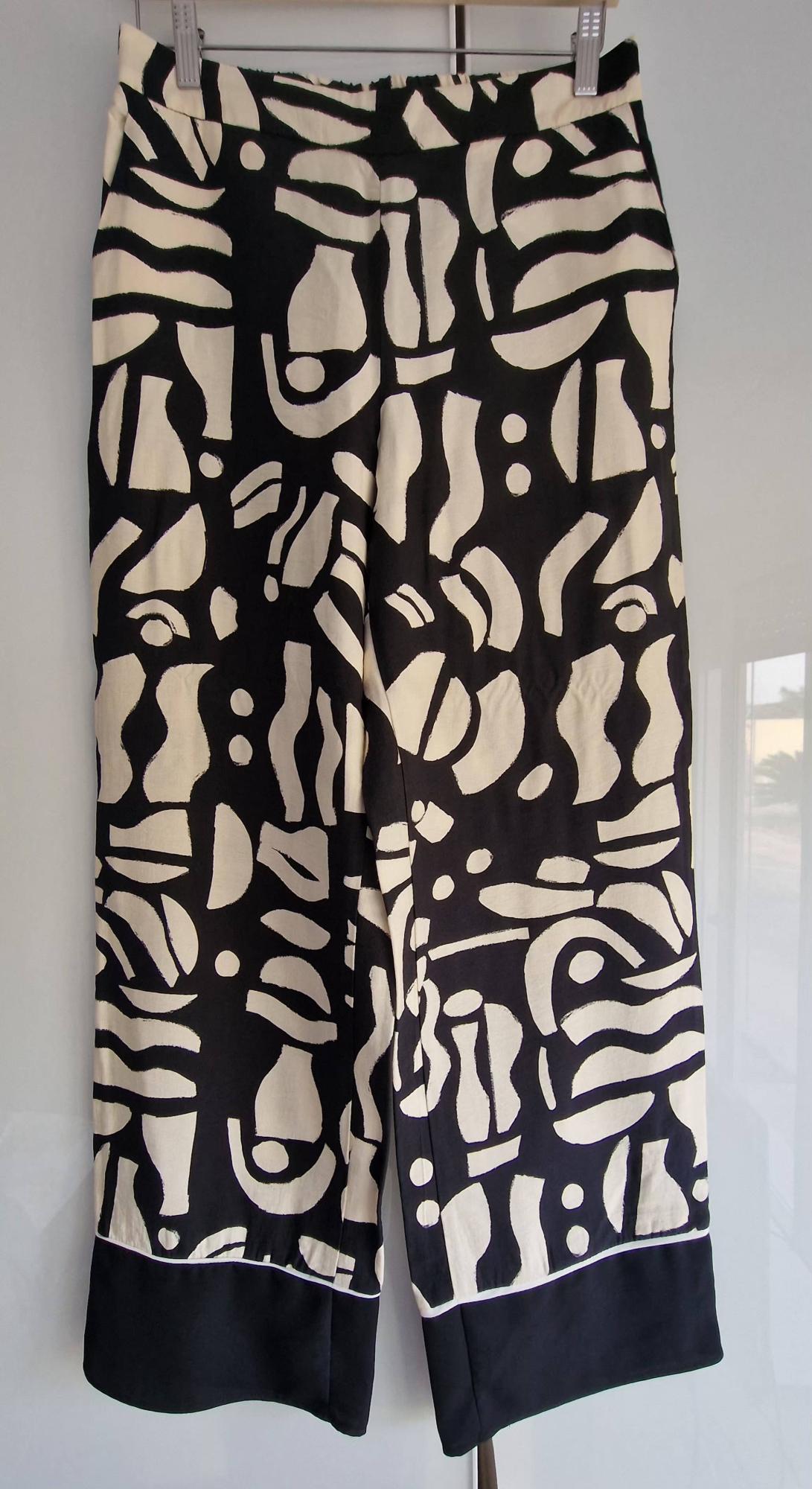 Trousers hanging on a hanger with an abstract black-and-white print of irregular shapes and a plain black hem with a thin white line.