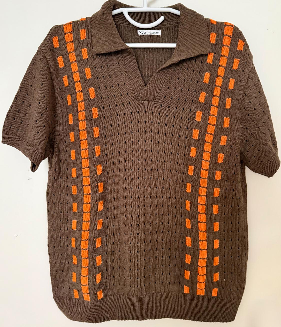 Brown jumper with orange line and check pattern, openwork knit, polo neck, hanging on a white hanger.