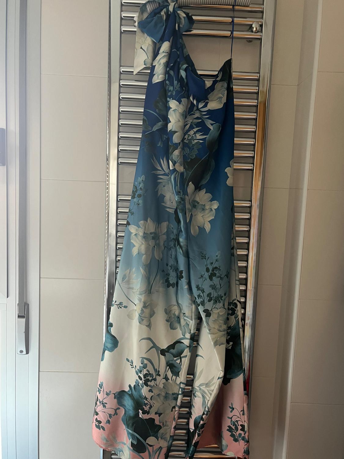Silk dress hanging on a radiator, with a floral print in shades of blue, white and pink. Interior setting with natural light.