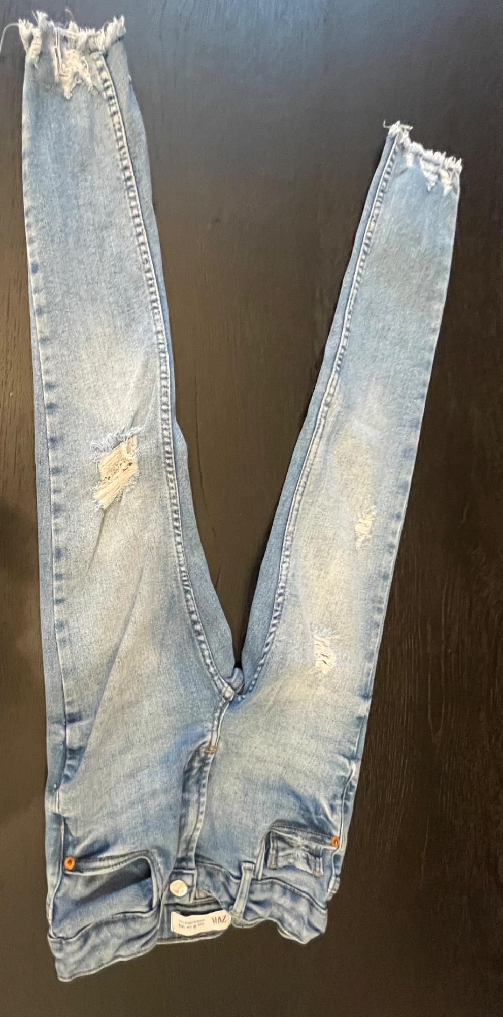 Light blue ripped jeans with frayed hems, placed upside down on a dark wooden surface. Text: ZARA.