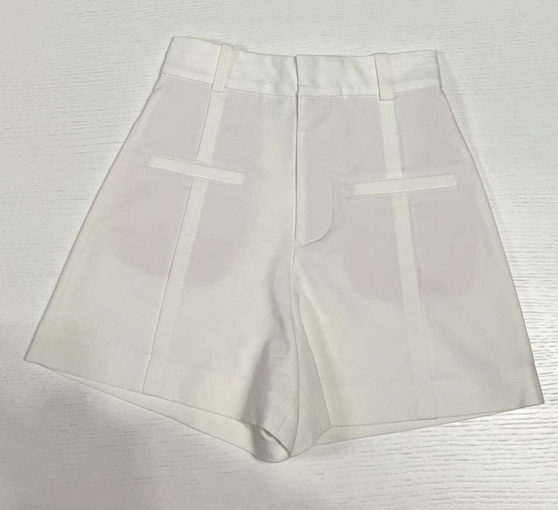 White shorts on a white background, with decorative back pockets and belt loops. Minimalist and clean style.