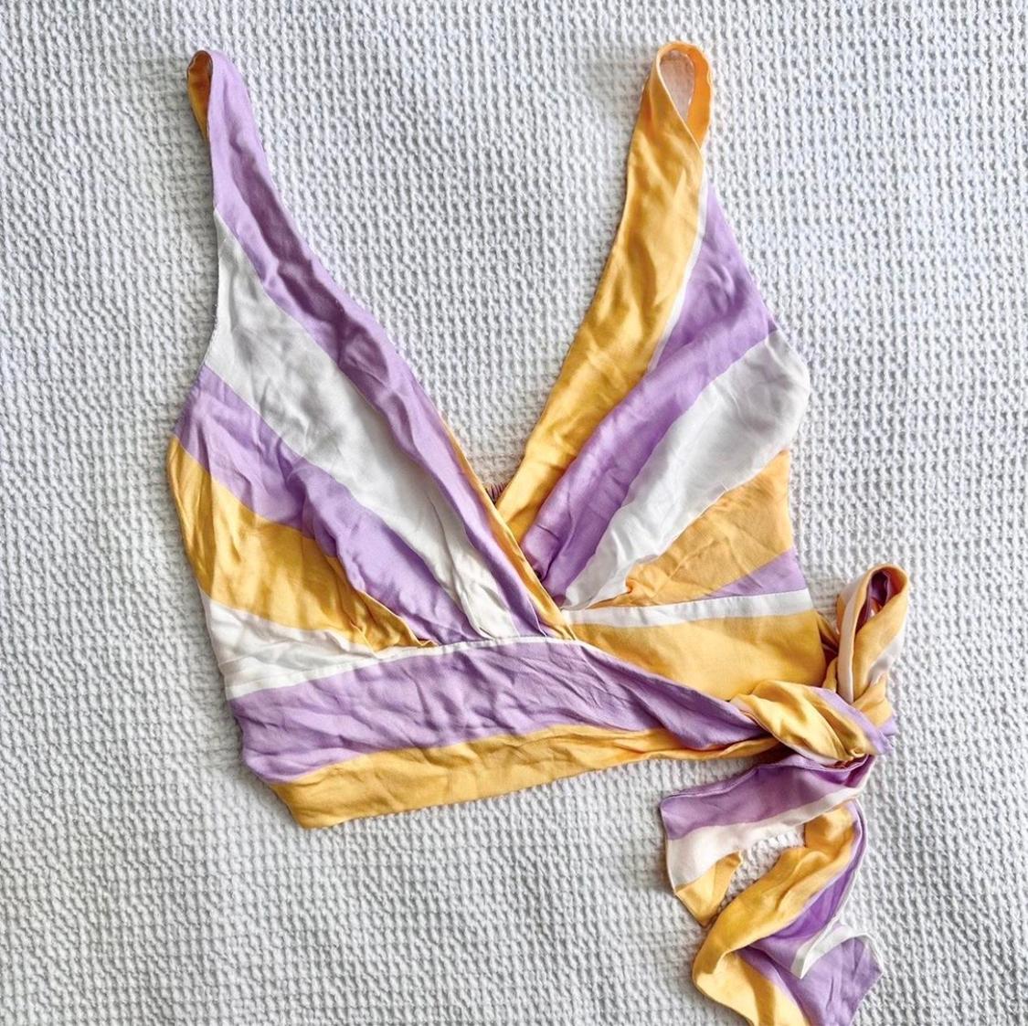 Lilac, white, and yellow criss-cross strap top, on a textured white background.