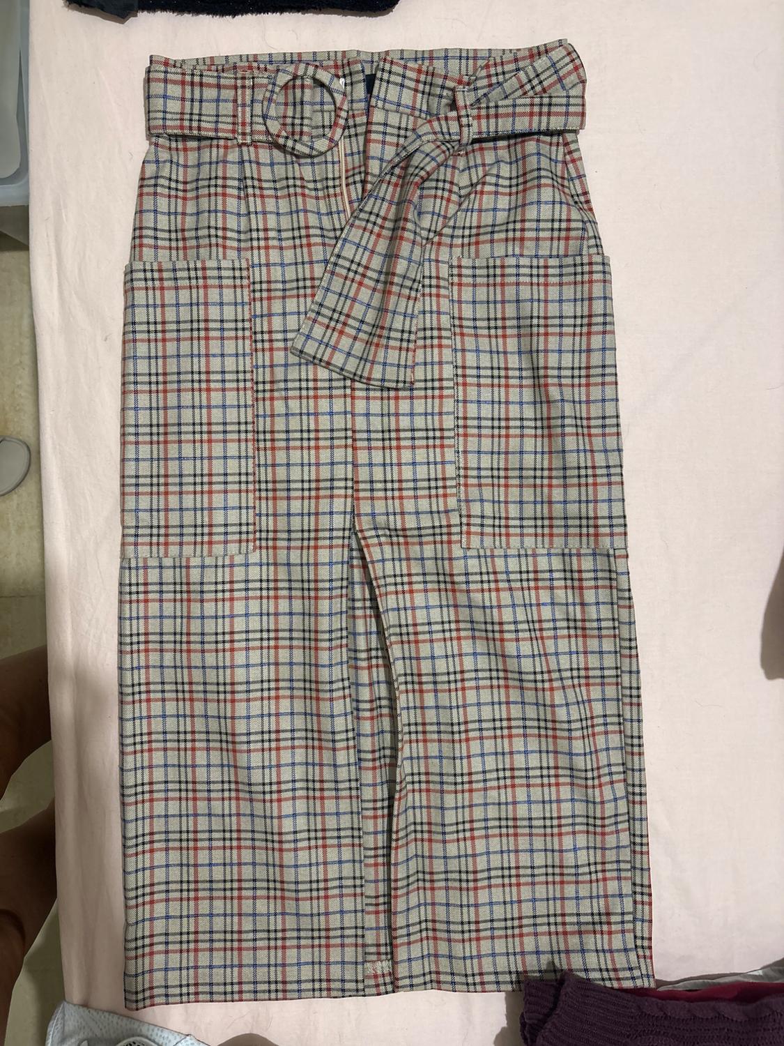 Checked midi skirt with matching belt, large front pockets and front split, photographed on a light sheet.