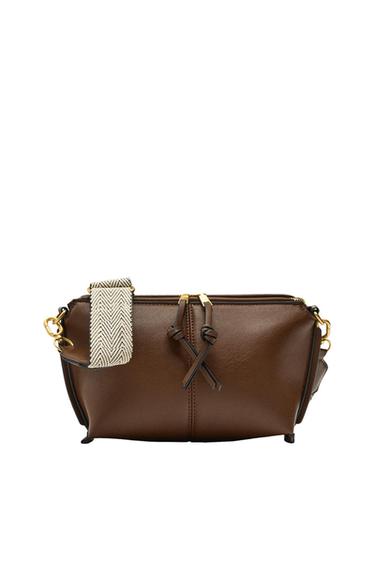 Brown handbag on a white background. It features a double zipper with knotted pulls and a wide, woven strap in a beige herringbone pattern.