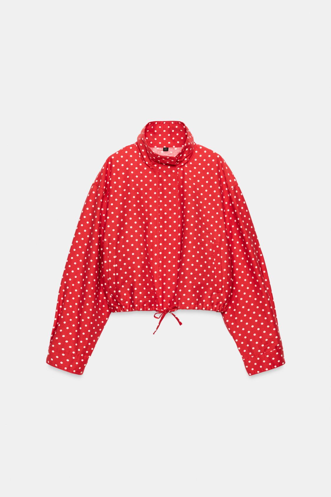 Front view of a red jacket with white polka dots, a round neck, long sleeves, and a drawstring hem.