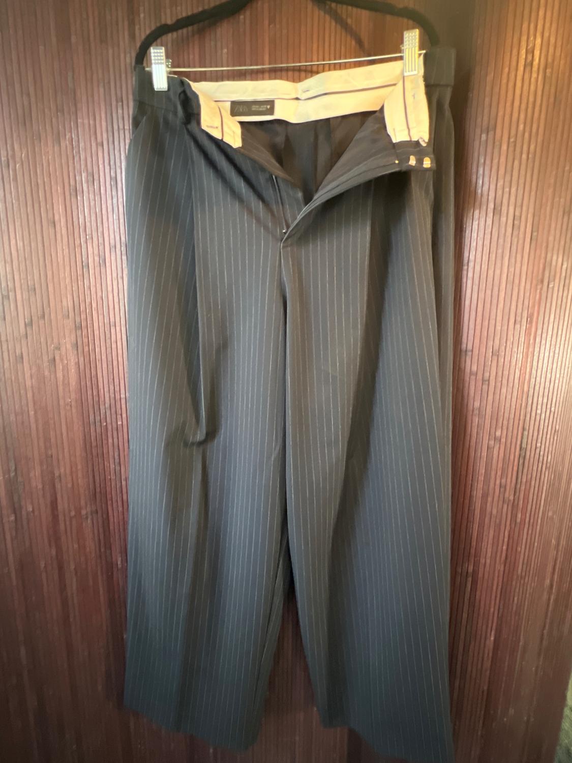 Dark-toned, vertical-striped dress pants hanging on a hanger against a brown wooden background.
