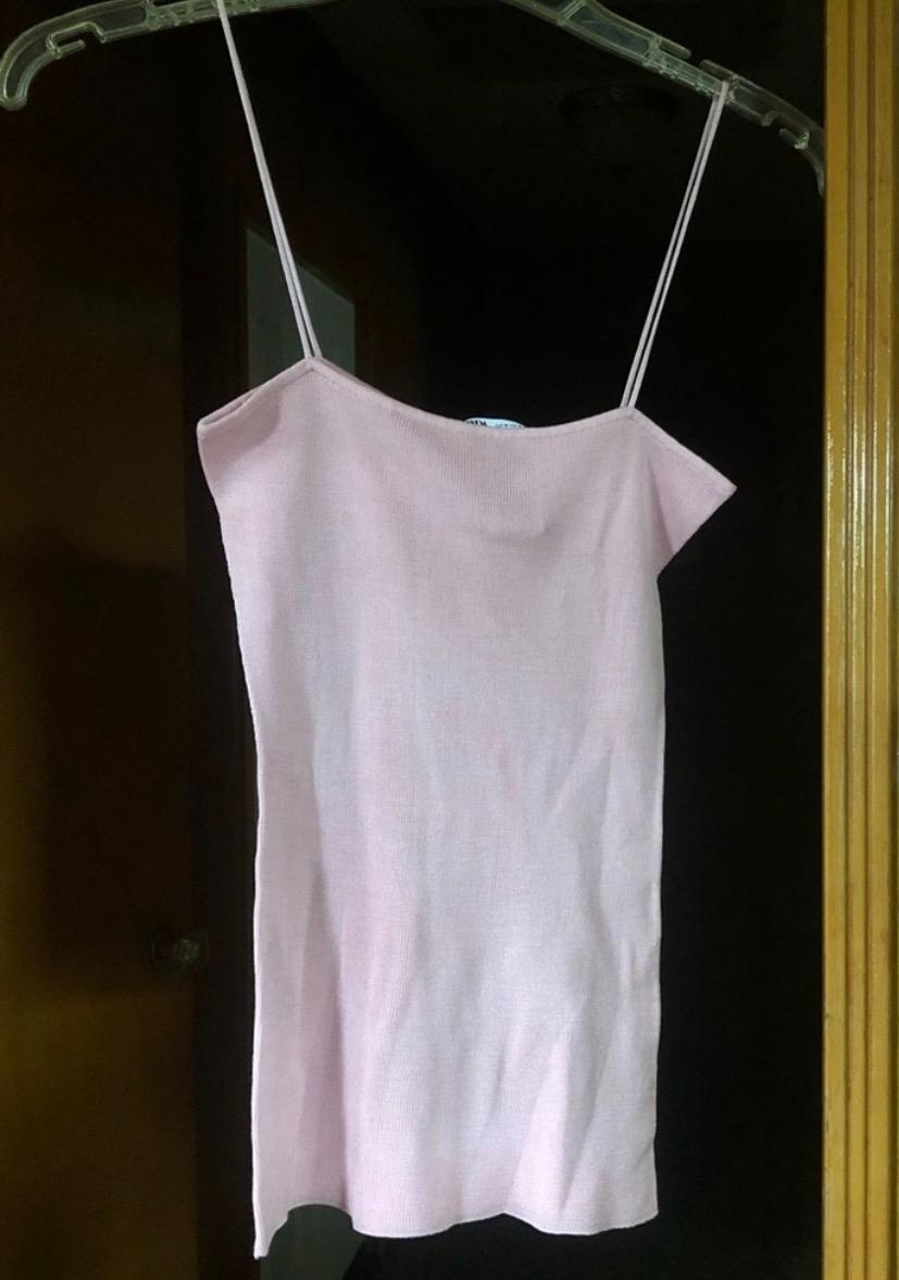 Light pink spaghetti strap dress hanging on a clear hanger, dark wood background, and white door.