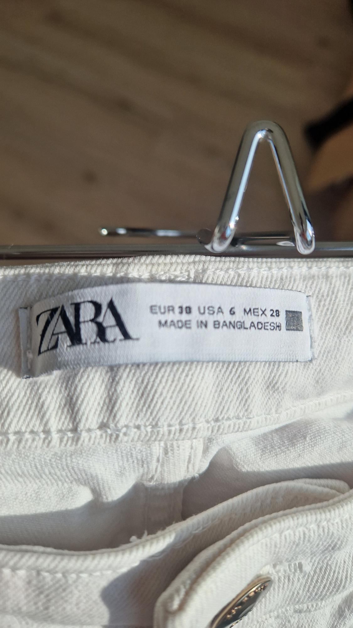 White trousers label with ZARA logo, sizes EUR 38, USA 6, MEX 28, made in Bangladesh, hanging on a metal hanger.