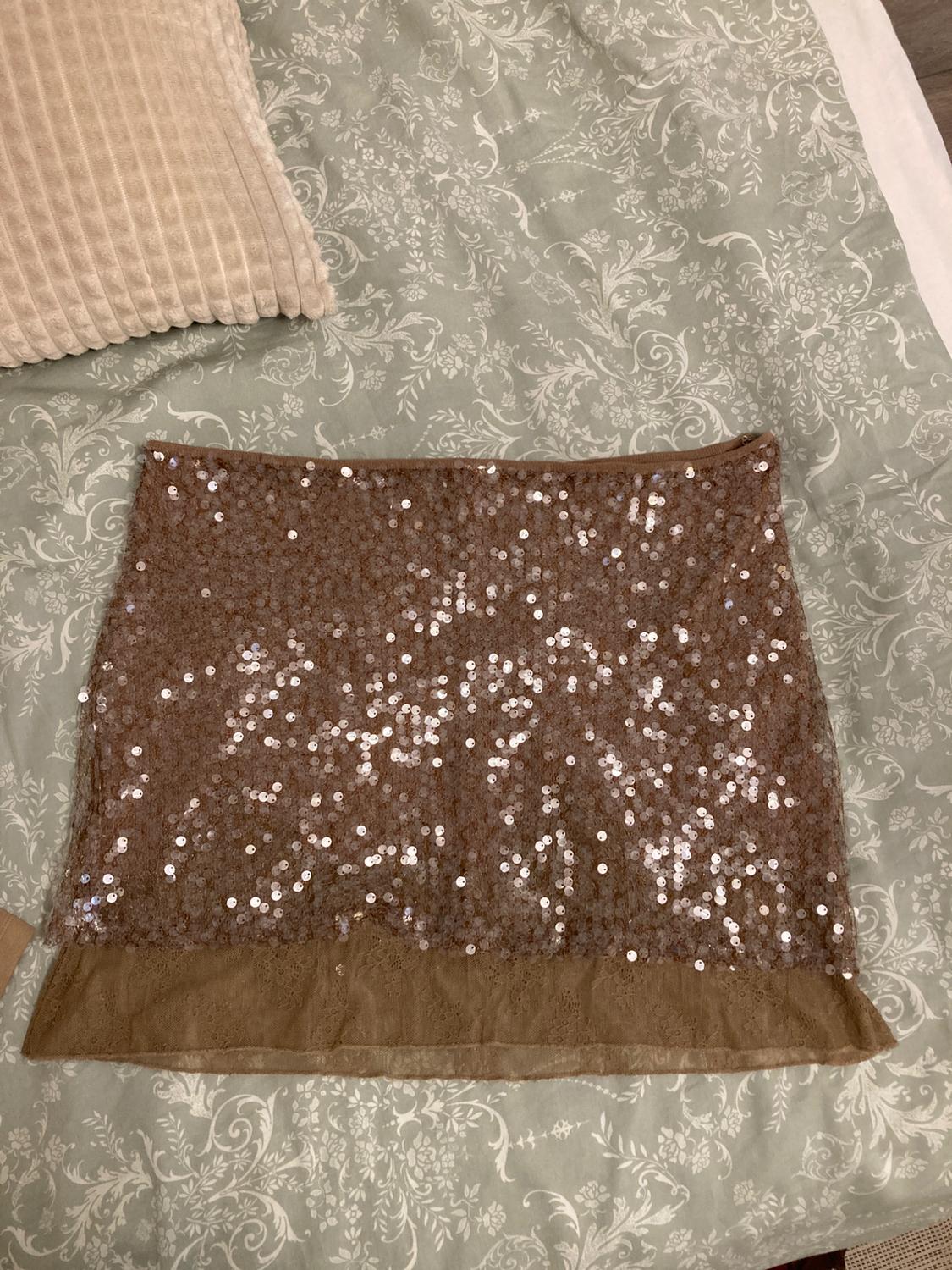 Brown sequin mini skirt with lace hem on a bed with green floral sheets and a beige cushion.
