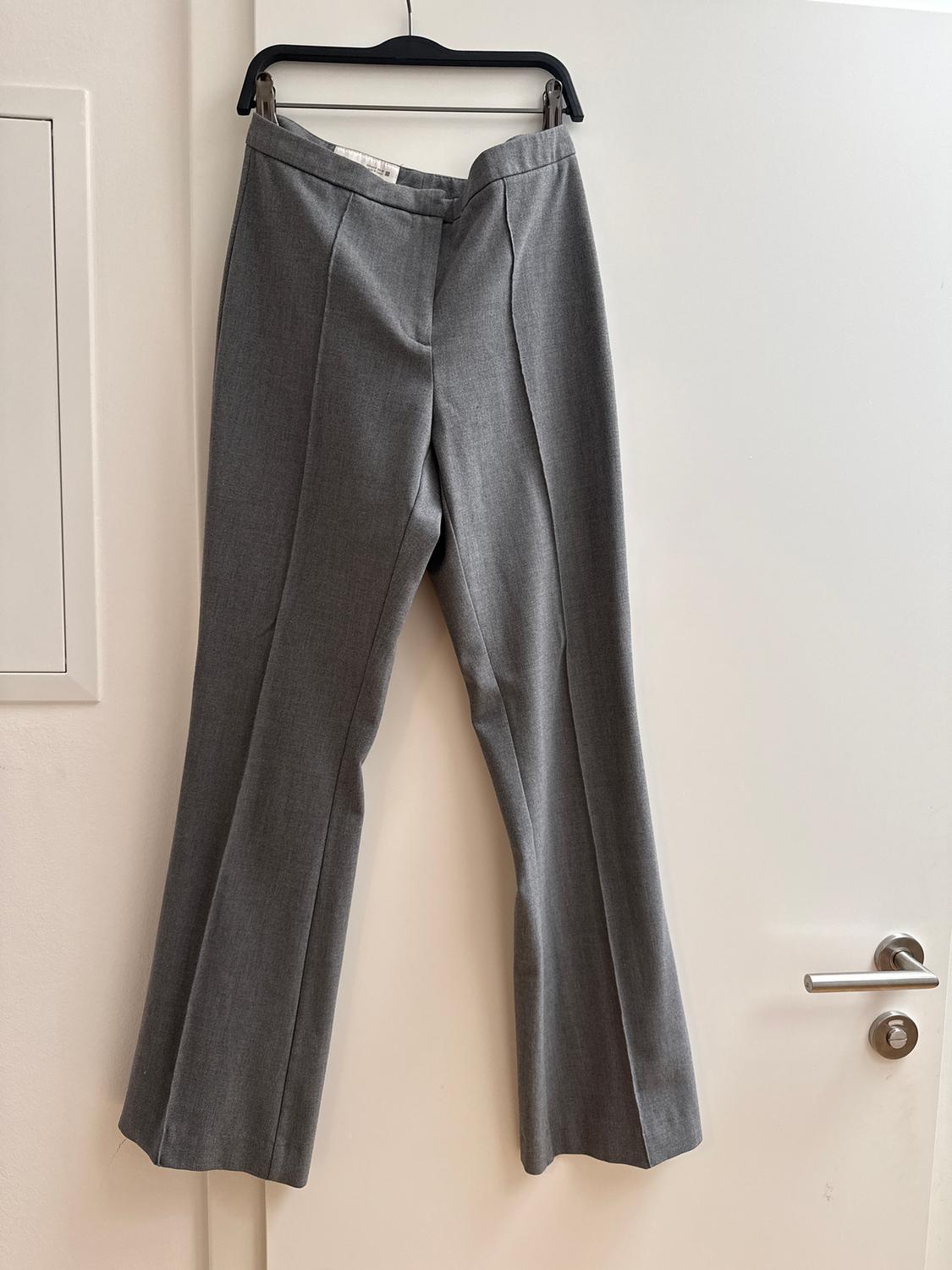 Grey dress trousers hanging on a black hanger over a white door. Wide-leg design with visible stitching.