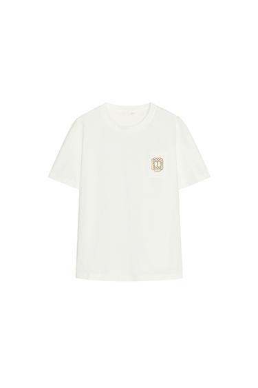 Front view of white t-shirt with pocket and gold graphic detail on the chest.