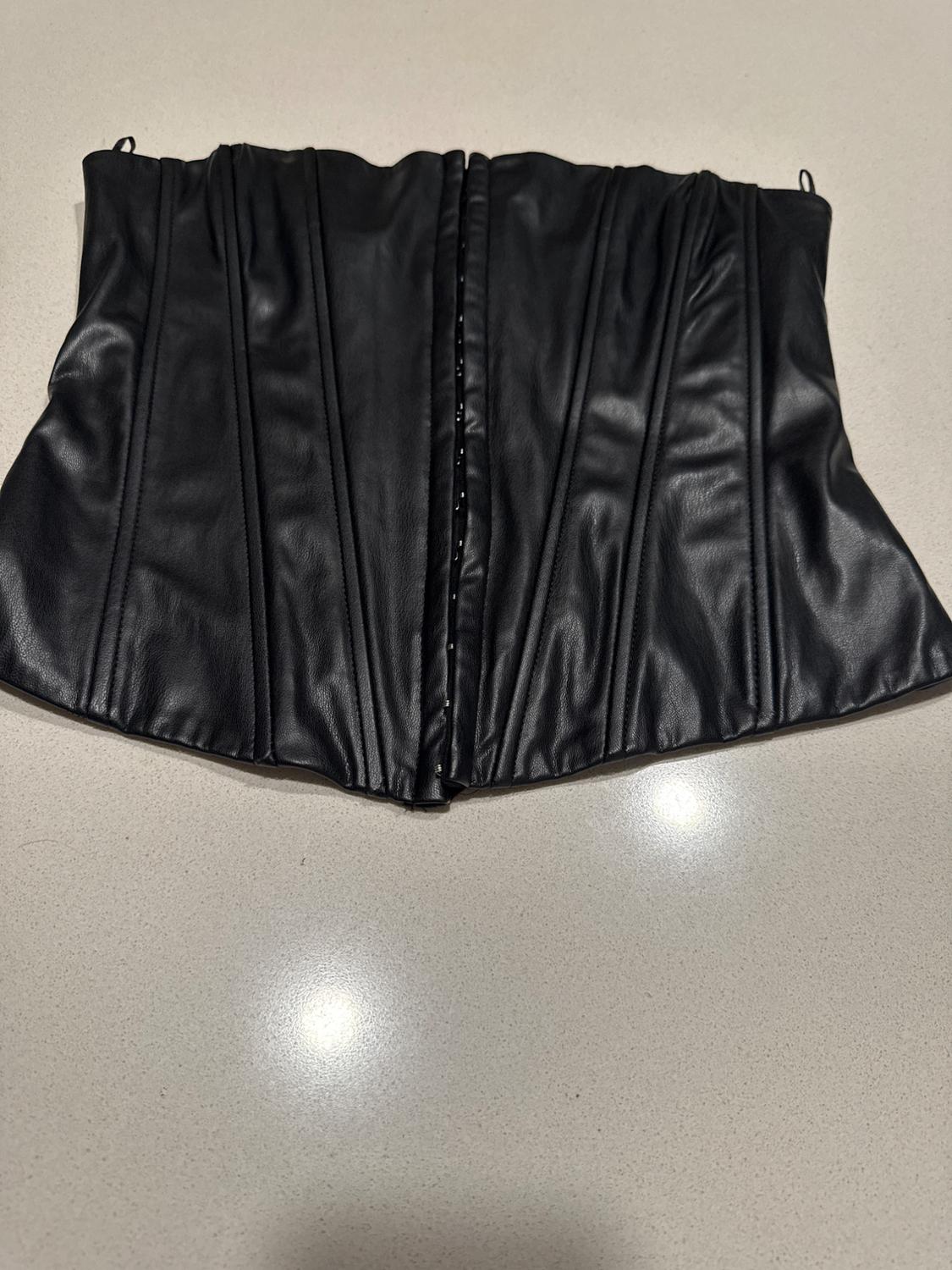 Black faux leather corset with vertical stitching on a light surface.