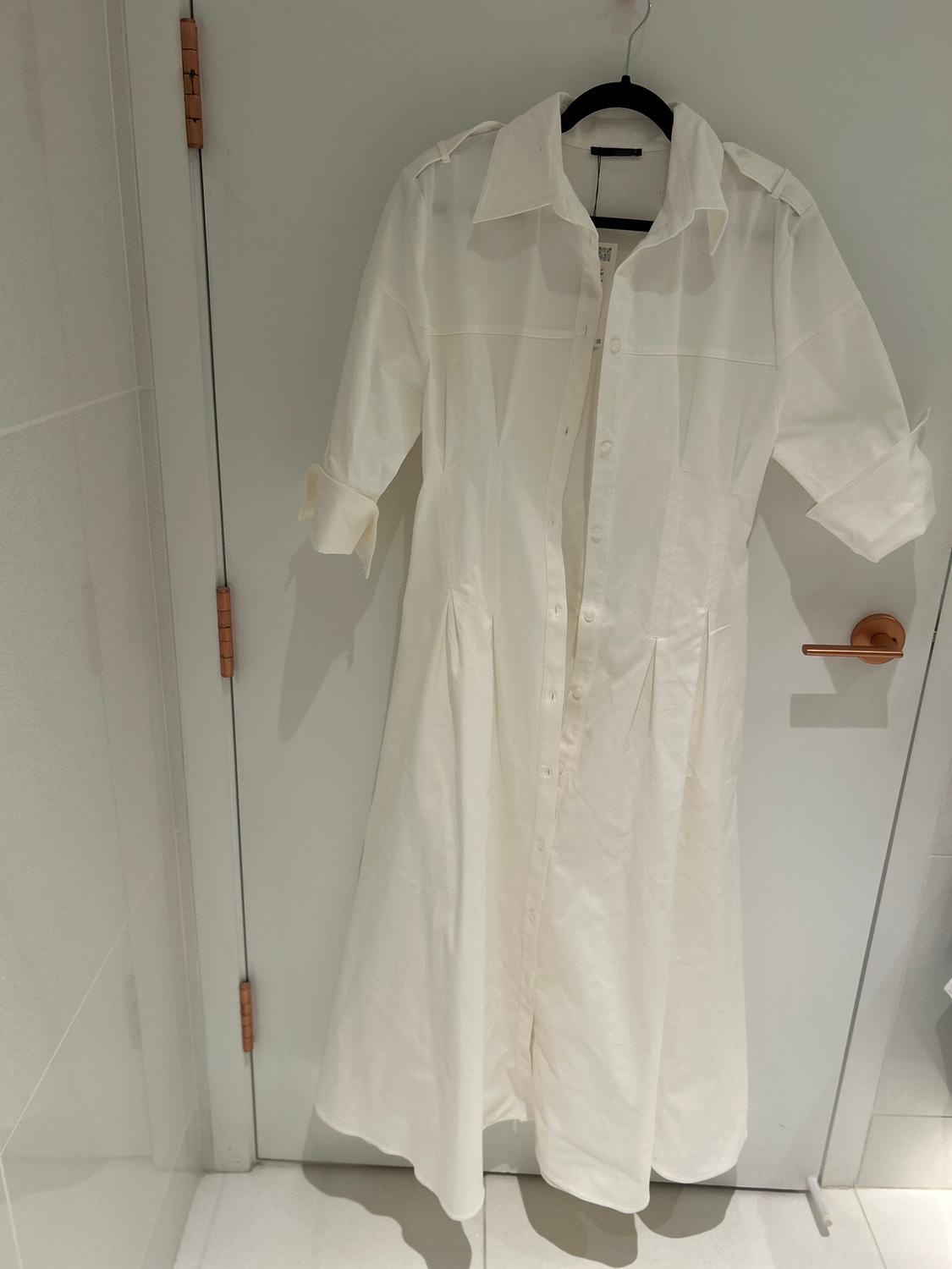 White, long-sleeved dress hanging on a black hanger over a white door. The door has a gold handle.