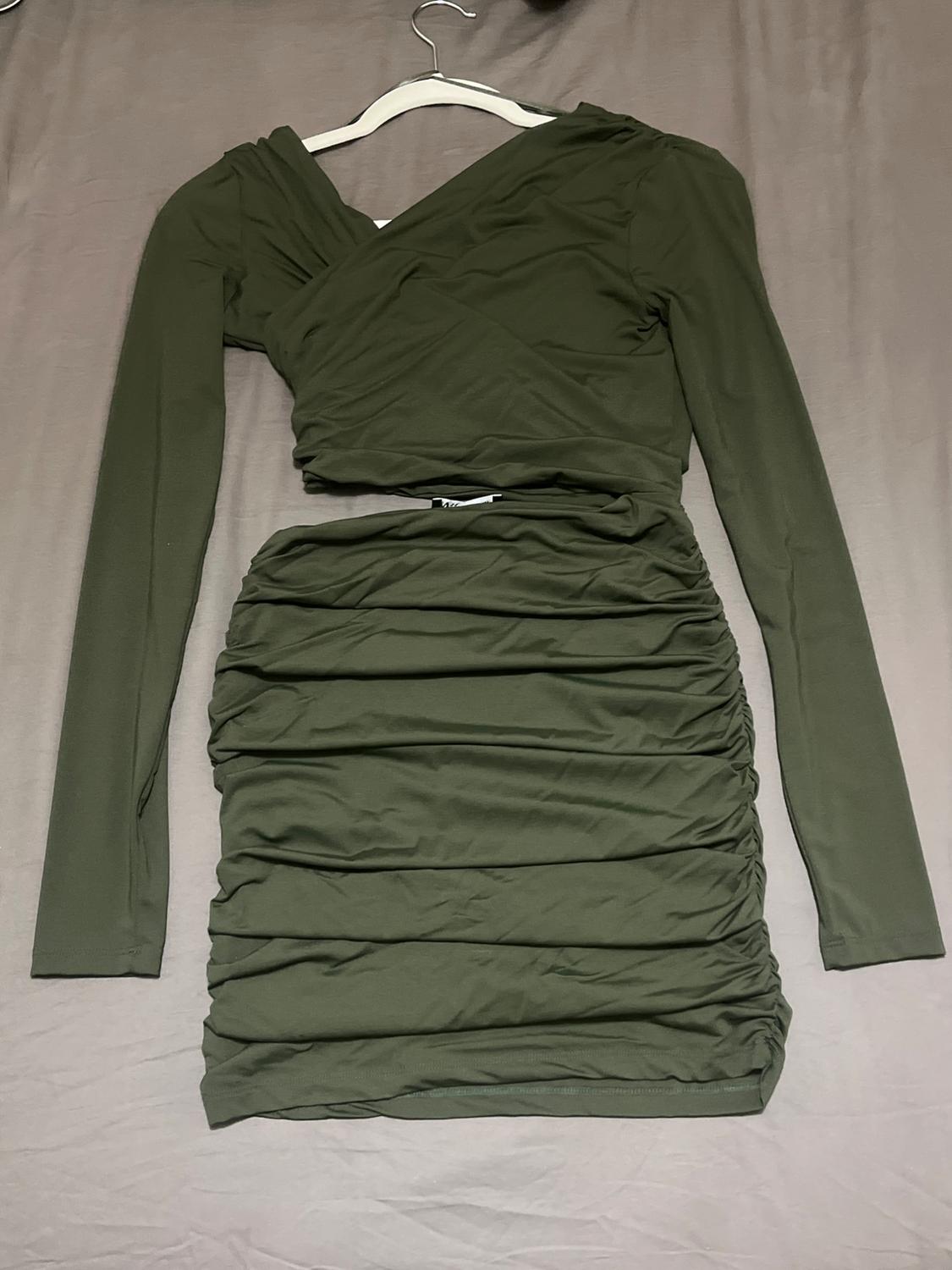 Olive green, long-sleeved dress with a ruched design, hanging on a hanger against a grey surface.