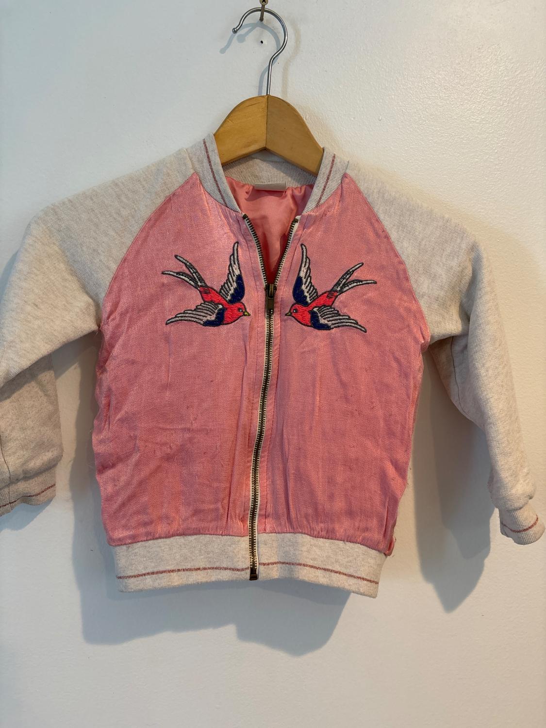 Front view of a pink jacket with bird embroidery on the chest and zipper.