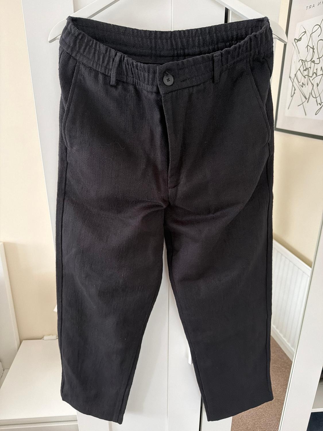 Black trousers hanging on a white hanger in front of a wardrobe. Background with a light wall and an abstract painting.