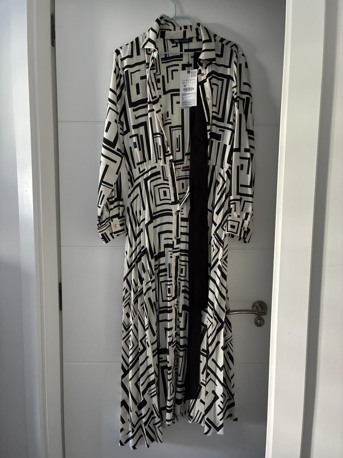 Long monochrome geometric-print shirt dress, hanging on a white door. Text: ZARA.