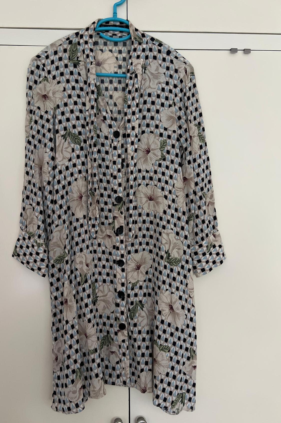 Front view of a floral and checked blouse with large buttons and long sleeves.
