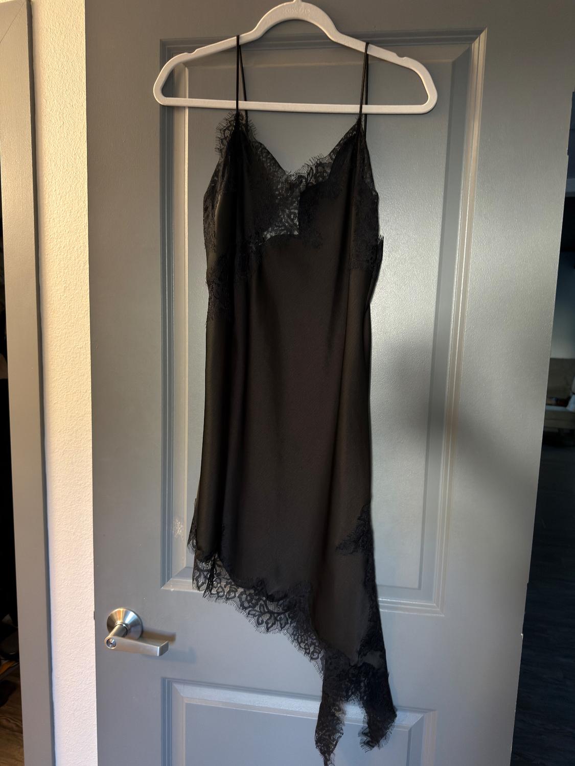 Black lace-trim camisole dress hanging on a white hanger over a grey door.