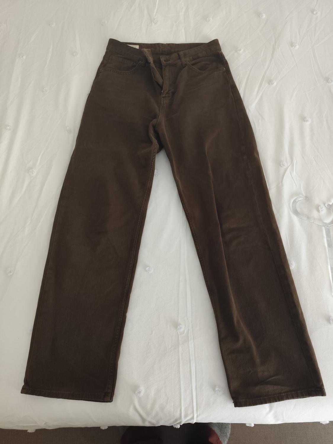 Brown straight-leg trousers on a white bed with button details.
