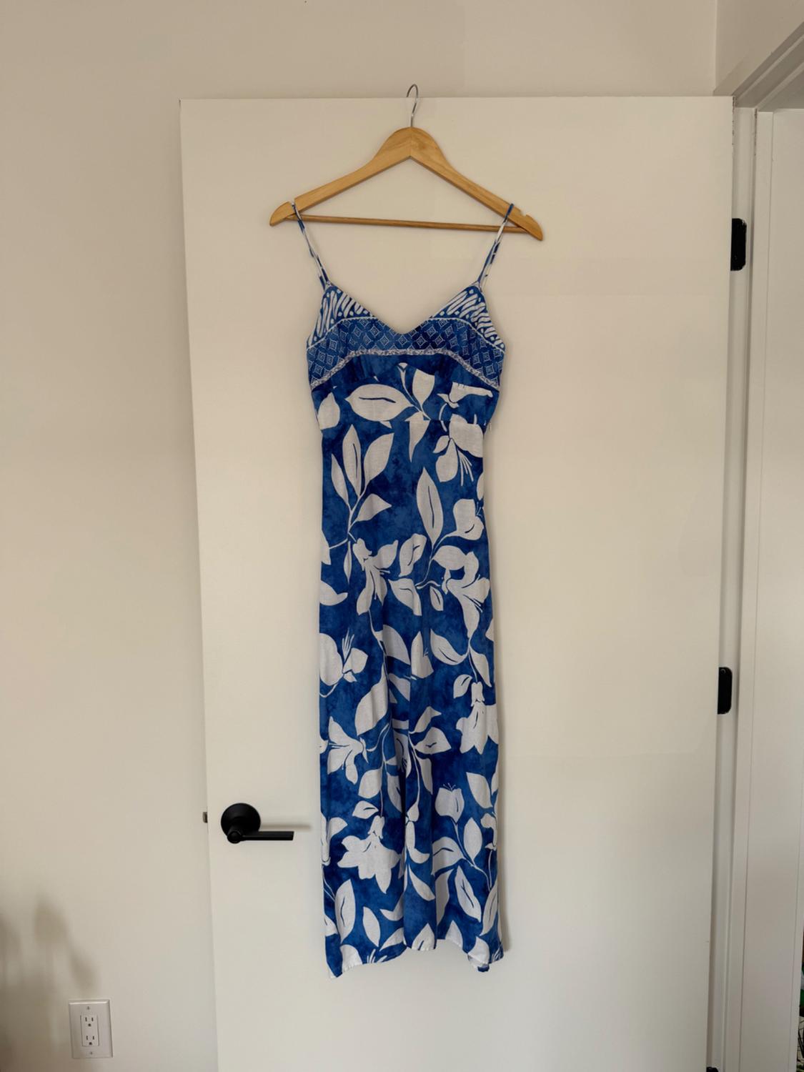 Long blue dress with a white leaf pattern, hanging on a wooden hanger over a white door.