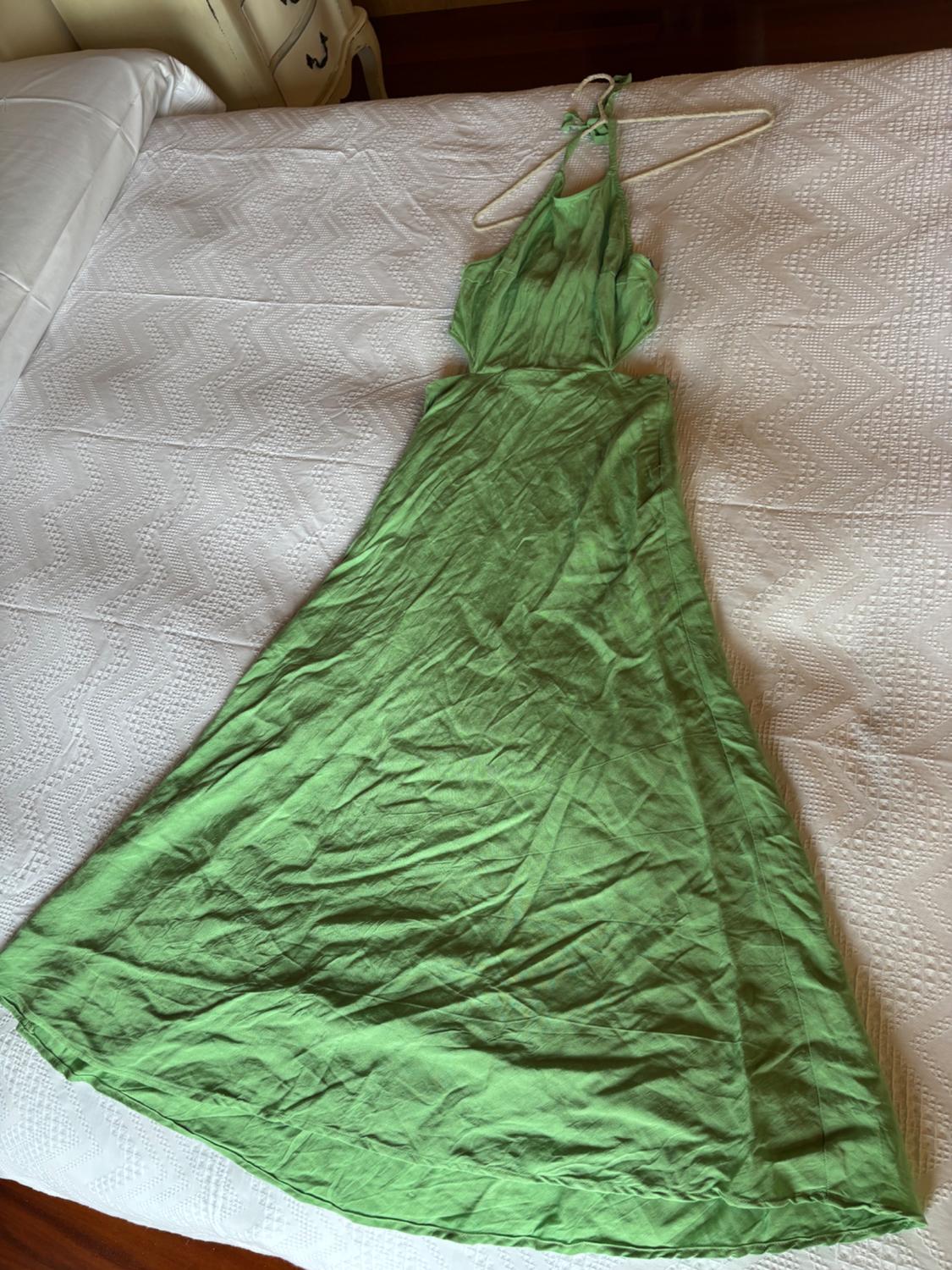 Long green dress with thin straps on a white bed with a geometric pattern bedspread.