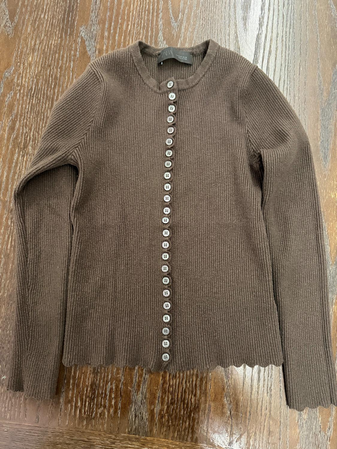 Brown knit cardigan with white buttons in the center, on a wooden surface.