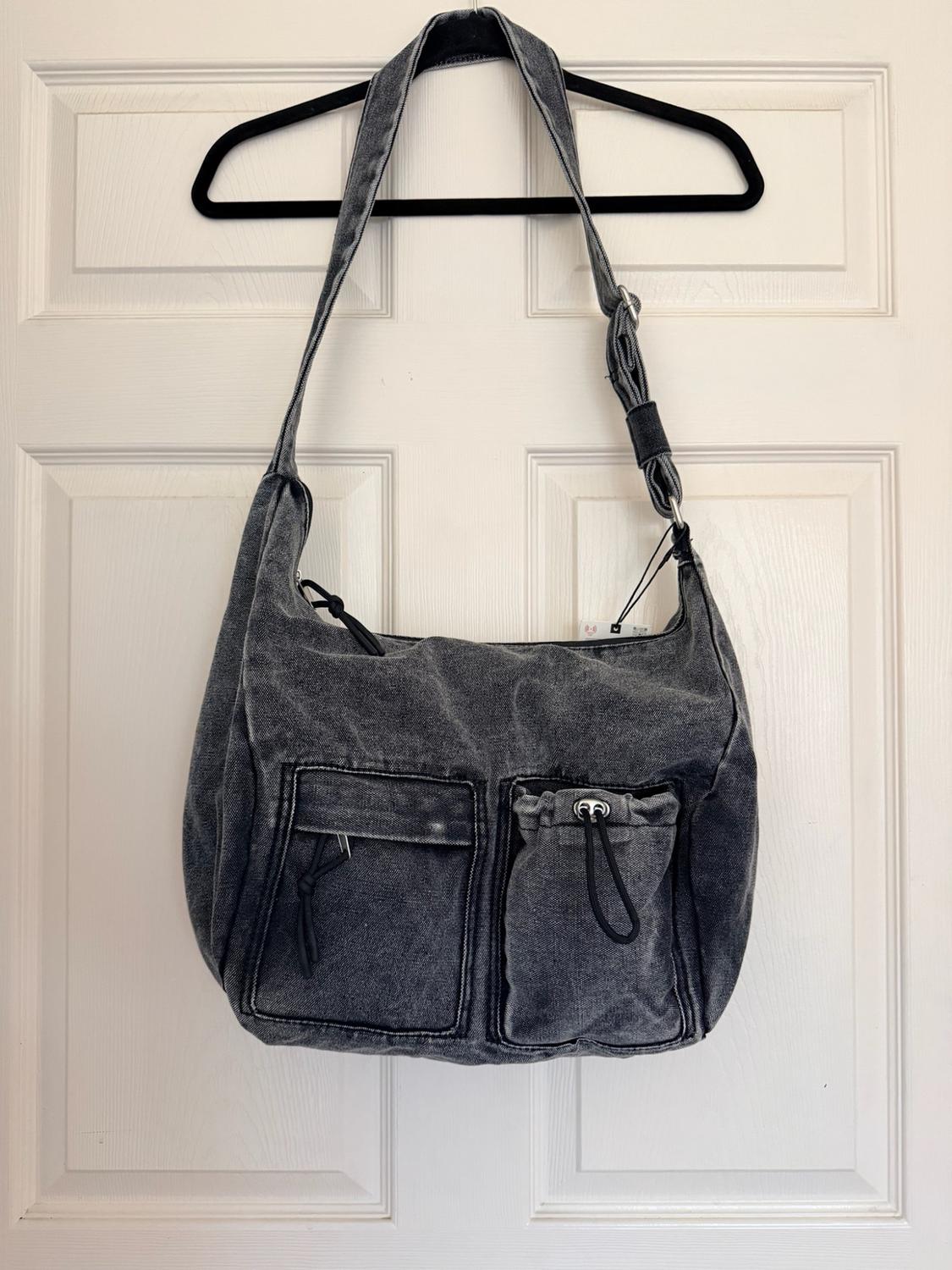 Washed grey denim bag with front pockets and cord pulls, hanging from a black hanger on a white door.