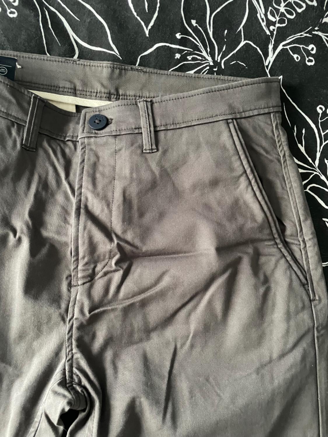 Grey trousers with front pockets and a dark button on a black background with a white floral design.