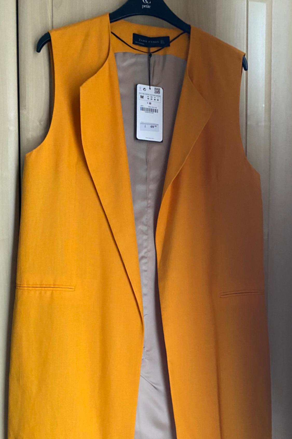 Front view of an orange sleeveless gilet with lapels and side pockets.
