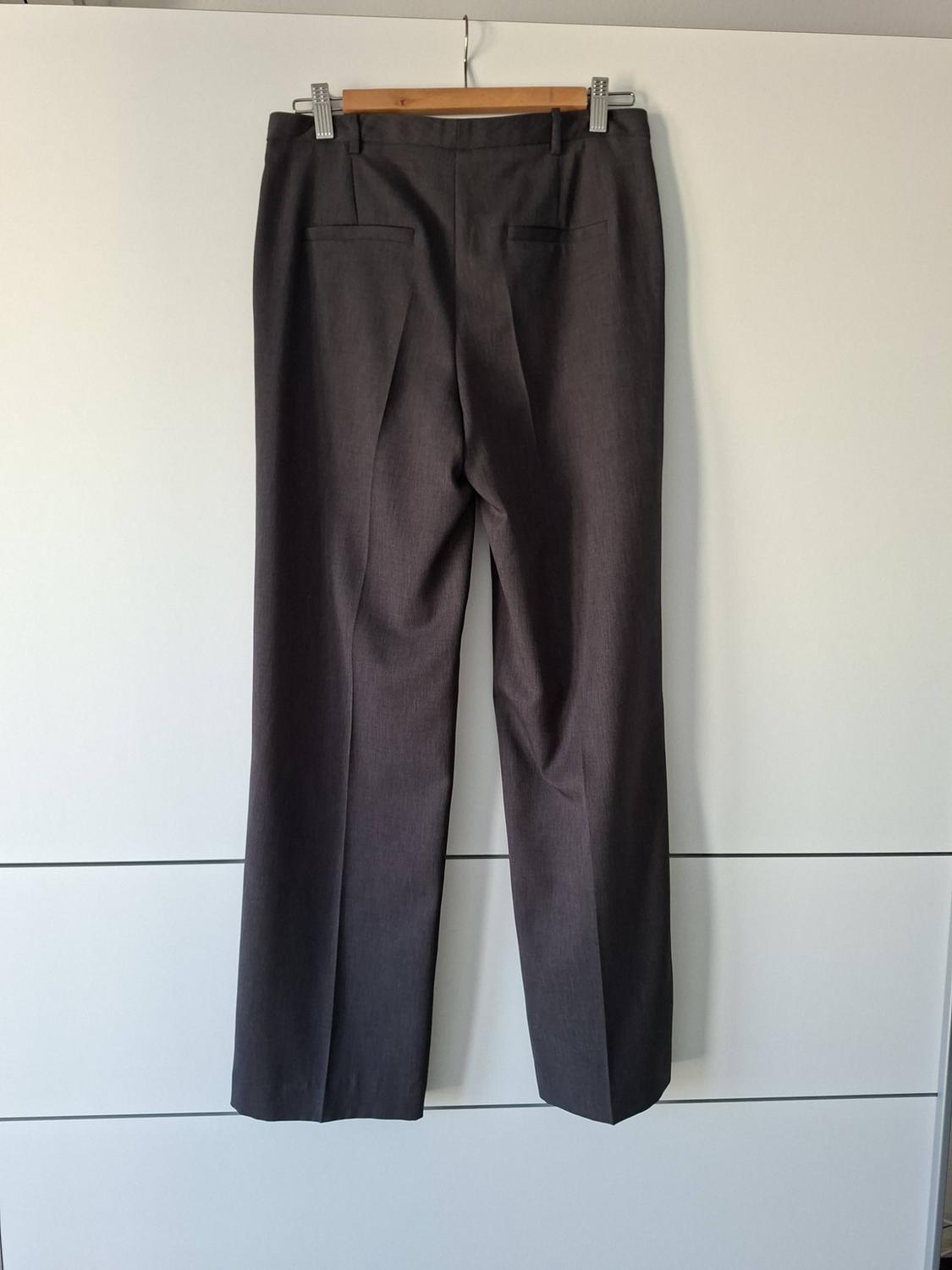 Rear view of dark grey dress trousers hanging on a wooden hanger against a white panelled background.