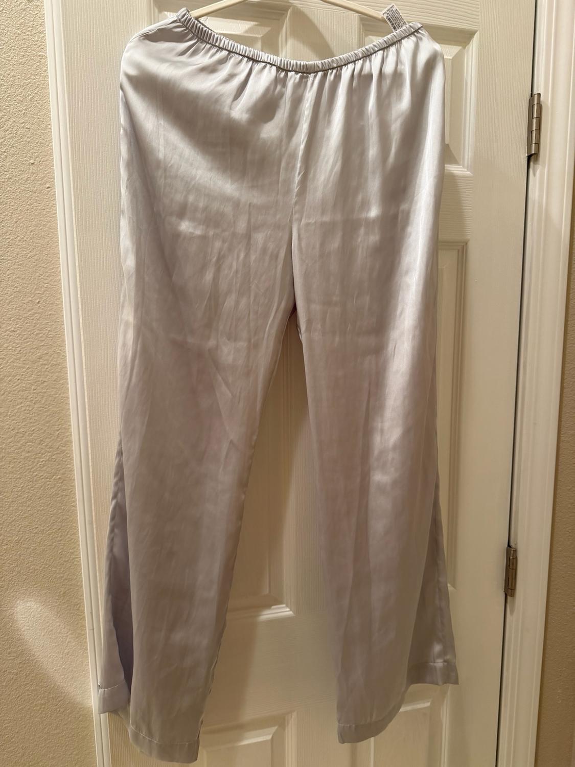 Light gray satin long pants with an elastic waistband, hanging on a hanger on a white door.