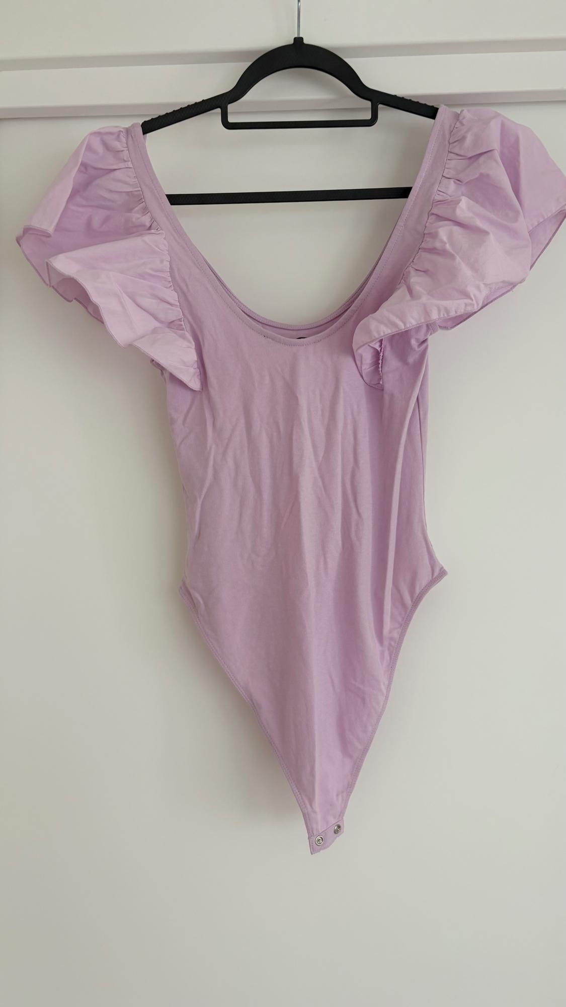 Lilac bodysuit with puffed sleeves hanging on a black hanger against a white background.