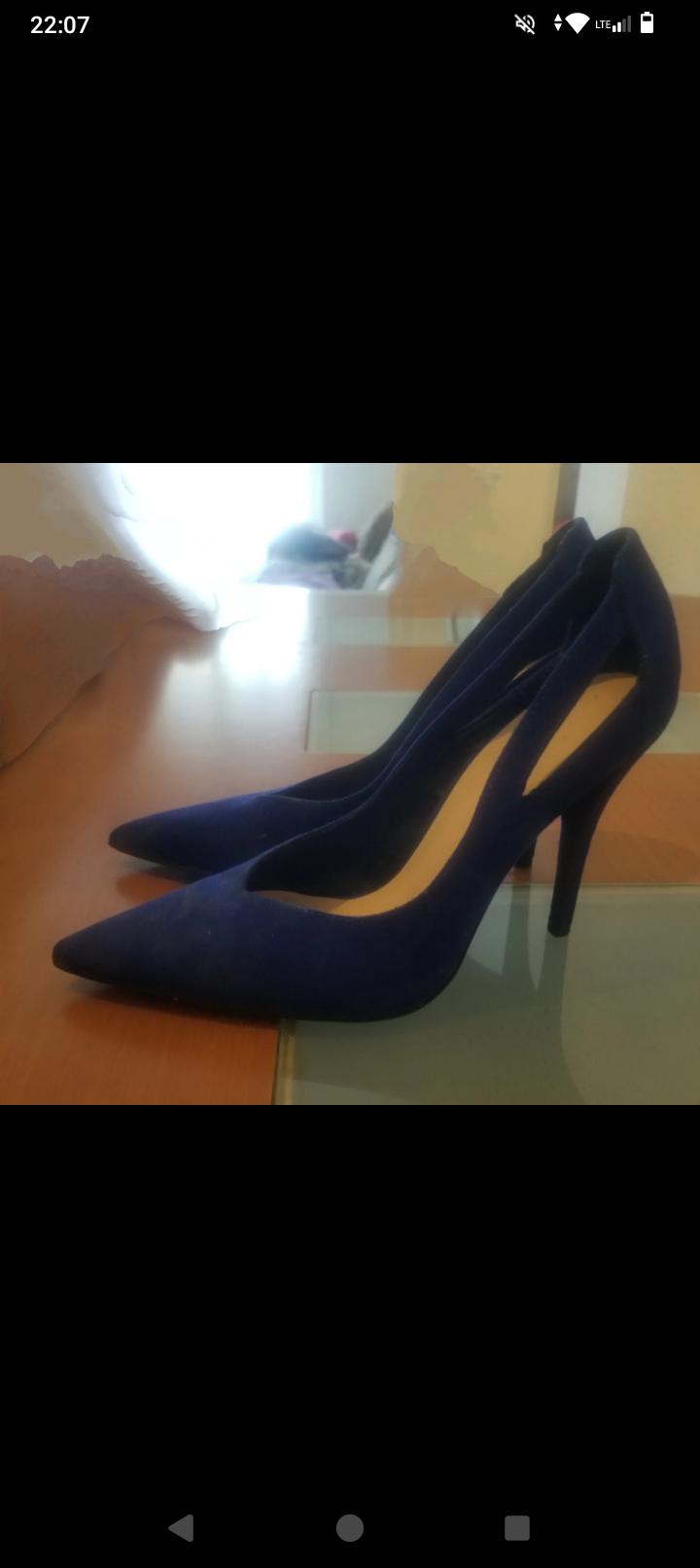 Dark blue high-heeled shoes with pointed toes on a wooden and glass table, illuminated by natural light.